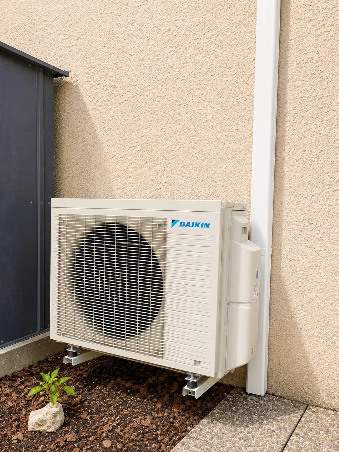 Groupe extérieur de climatisation Daikin installé en fond de jardin, à côté d’un abri